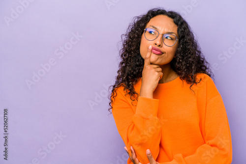 Young hispanic woman isolated on purple background looking sideways with doubtful and skeptical expression. photo