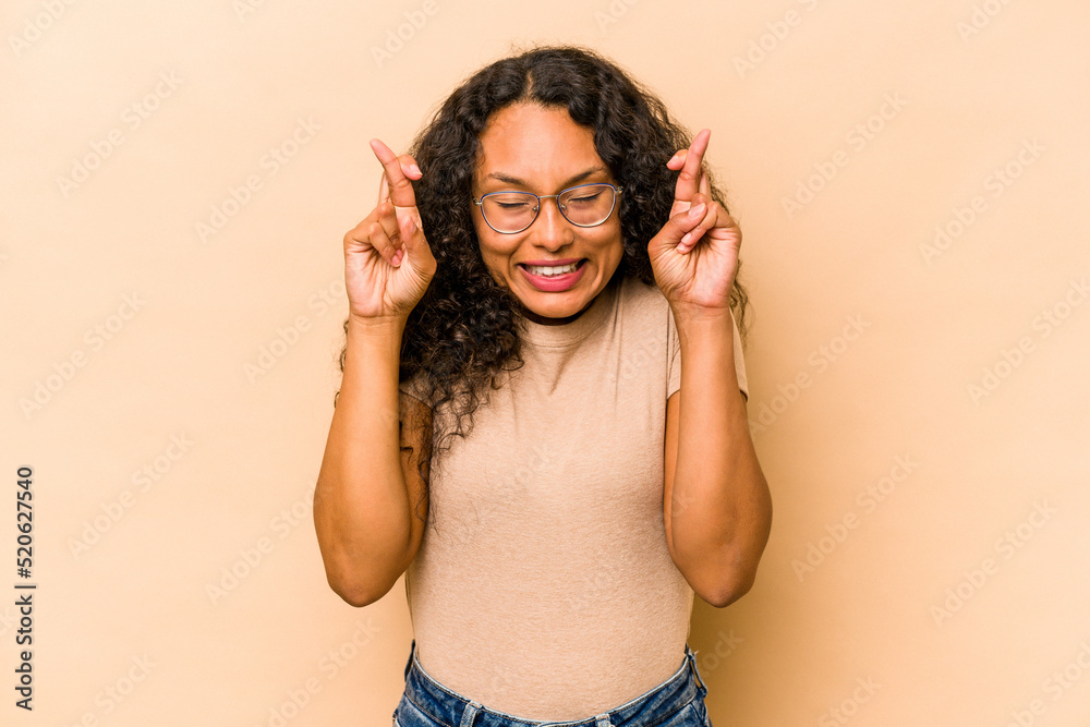 Fototapeta premium Young hispanic woman isolated on beige background crossing fingers for having luck