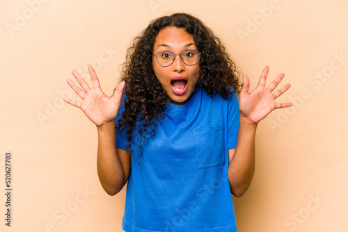 Young hispanic woman isolated on beige background receiving a pleasant surprise, excited and raising hands. © Asier