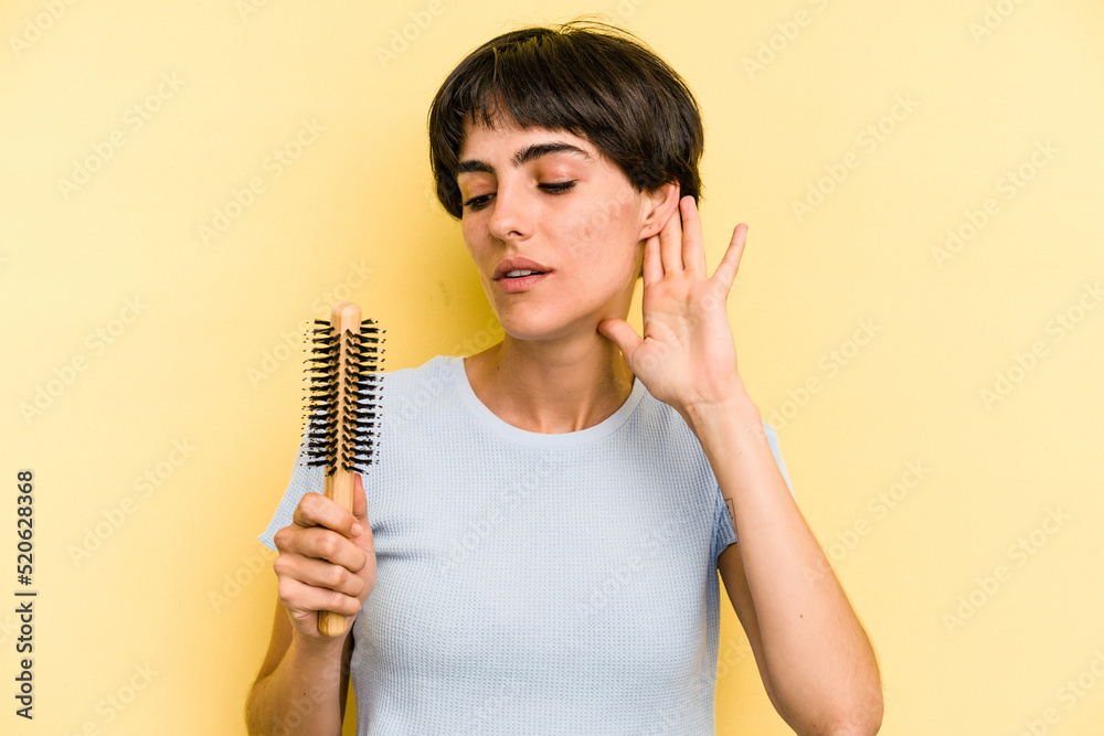 Young caucasian woman holding a brush hair isolated on yellow background trying to listening a gossip. Young caucasian woman holding a brush hair isolated on yellow background trying to listening a gossip.