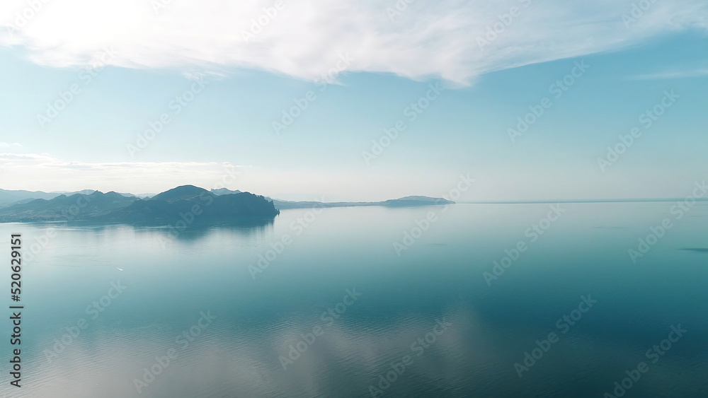 Mirrored water reflects blue sky with mountain horizon. Shot. Picturesque landscape with reflection of blue sky in quiet surface of sea. Merging sea and sky are separated by mountain horizon