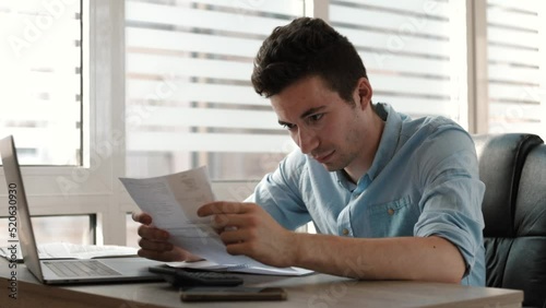accountant doing calculation for online financial report at workplace. Serious man using calculator paying bill online holding paper sitting at home office desk. Accounting concept