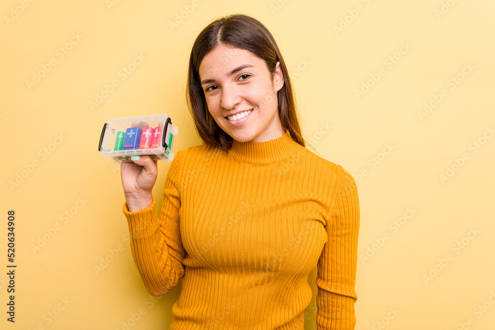 Young caucasian woman holding a batteries box isolated on yellow background happy, smiling and cheerful. Young caucasian woman holding a batteries box isolated on yellow background happy, smiling and cheerful.