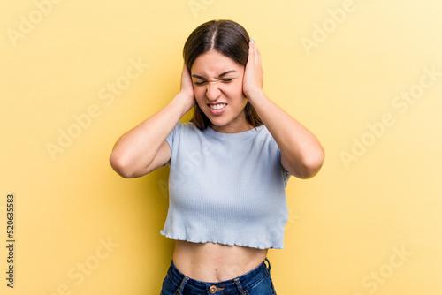 Young caucasian woman isolated on yellow background covering ears with hands.