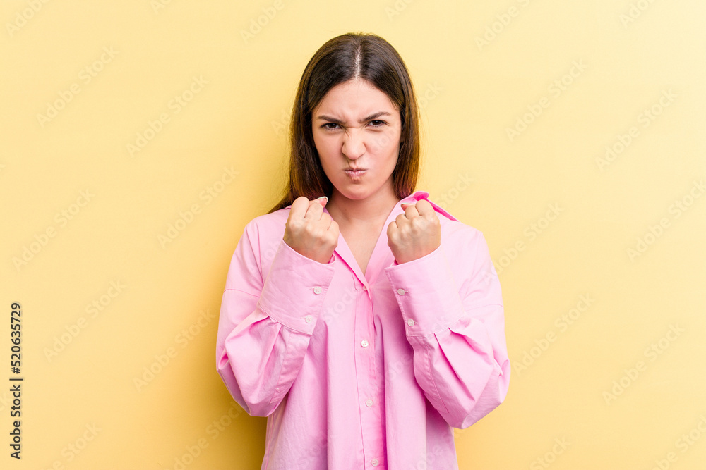 Young caucasian woman isolated on yellow background showing fist to camera, aggressive facial expression. Young caucasian woman isolated on yellow background showing fist to camera, aggressive facial expression.
