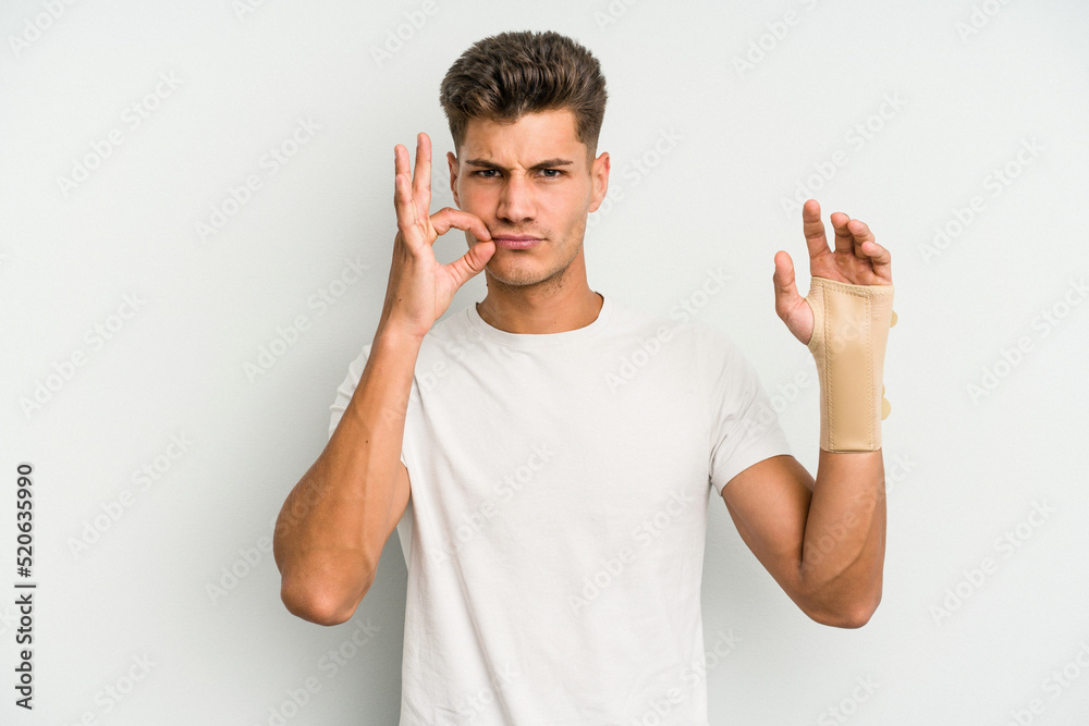 Young caucasian man hand sling isolated on white background with fingers on lips keeping a secret.
