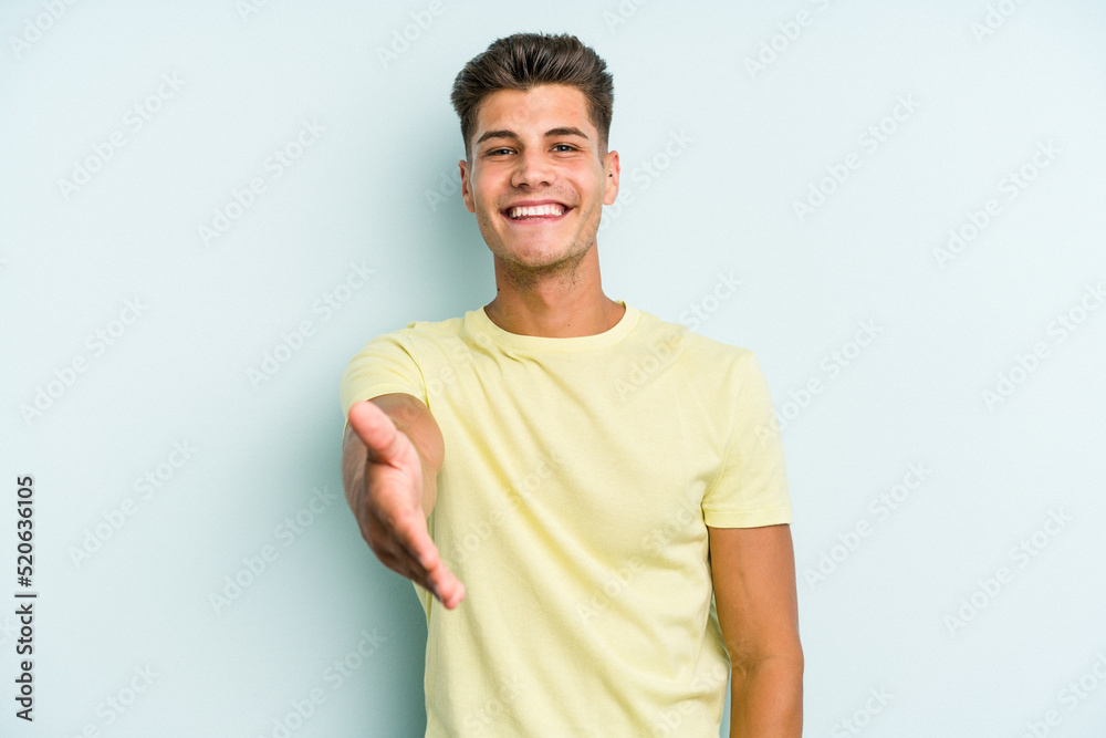 Obraz premium Young caucasian man isolated on blue background stretching hand at camera in greeting gesture.