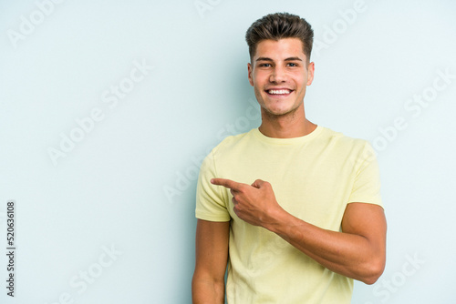 Young caucasian man isolated on blue background smiling and pointing aside, showing something at blank space.