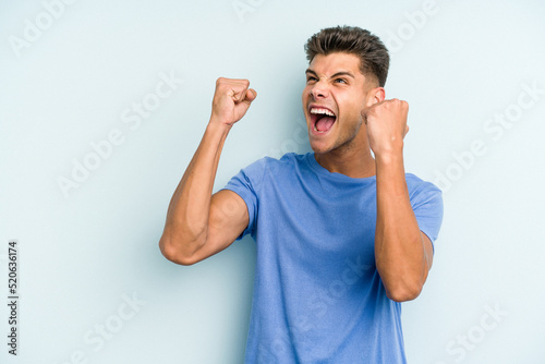 Young caucasian man isolated on blue background raising fist after a victory, winner concept.