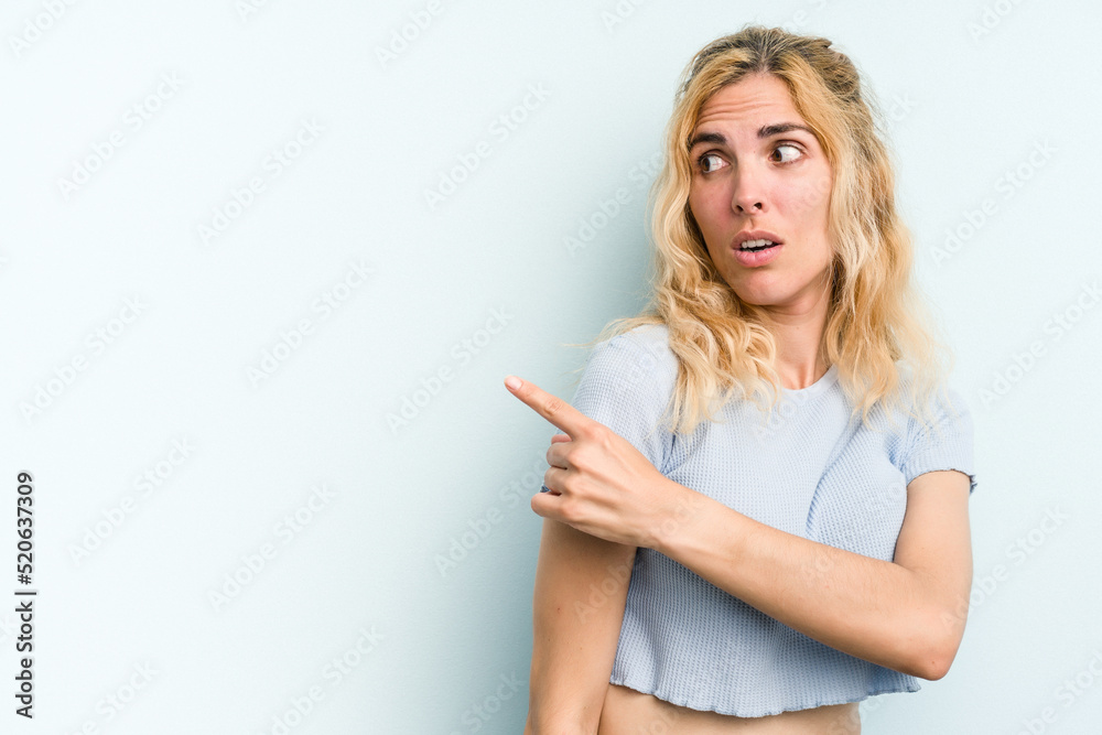 Young caucasian woman isolated on blue background smiling and pointing aside, showing something at blank space. Young caucasian woman isolated on blue background smiling and pointing aside, showing something at blank space.