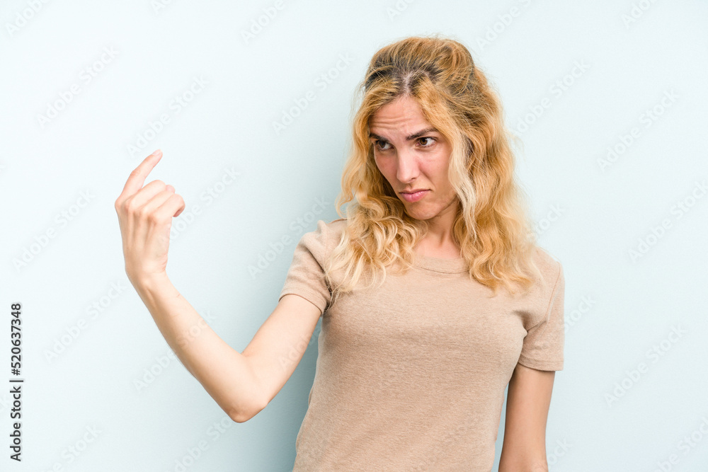 Young caucasian woman isolated on blue background pointing with finger at you as if inviting come closer. Young caucasian woman isolated on blue background pointing with finger at you as if inviting come closer.