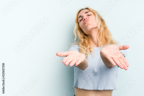 Young caucasian woman isolated on blue background folding lips and holding palms to send air kiss.