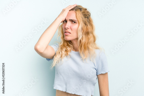 Young caucasian woman isolated on blue background forgetting something, slapping forehead with palm and closing eyes.