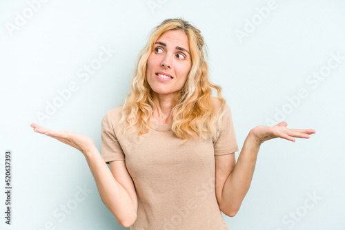 Young caucasian woman isolated on blue background confused and doubtful shrugging shoulders to hold a copy space.