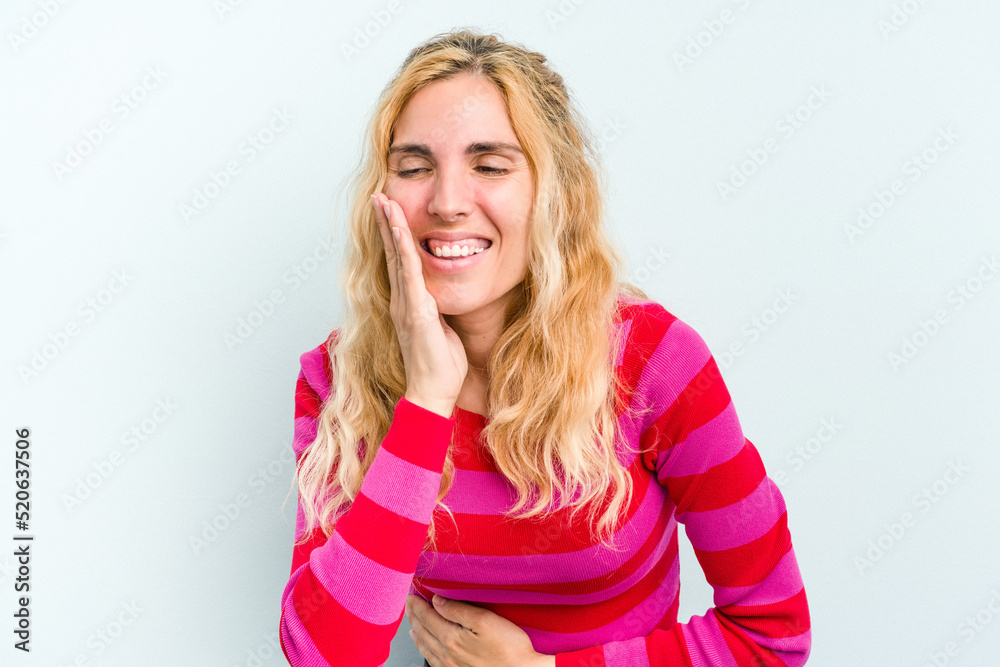 Young caucasian woman isolated on blue background laughs happily and has fun keeping hands on stomach. Young caucasian woman isolated on blue background laughs happily and has fun keeping hands on stomach.