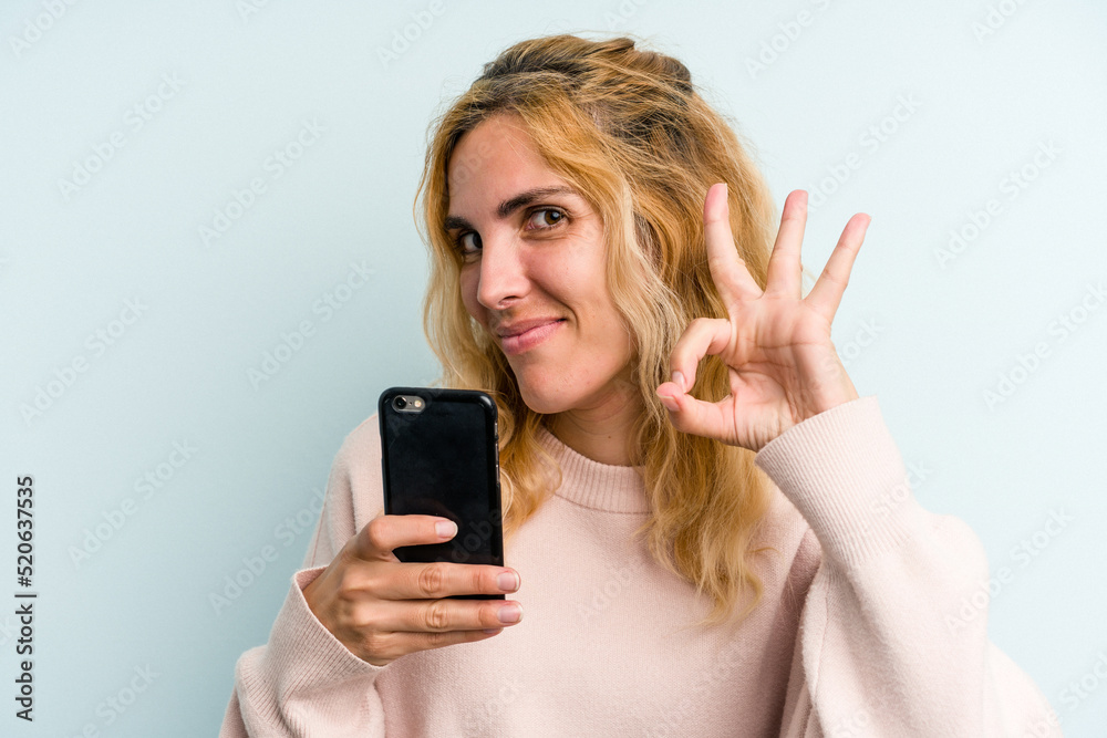 Young caucasian woman holding mobile phone isolated on blue background Young caucasian woman holding mobile phone isolated on blue background