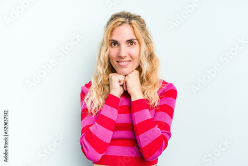 Young caucasian woman isolated on blue background keeps hands under chin, is looking happily aside.