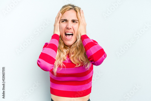 Young caucasian woman isolated on blue background covering ears with hands trying not to hear too loud sound. © Asier