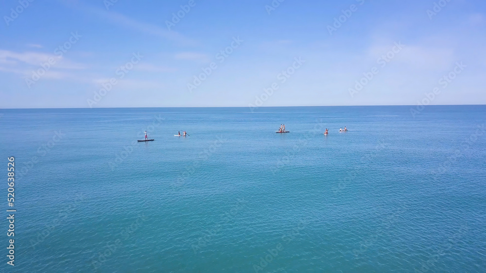 Group of people swim on SUP Board. Clip. Beautiful seascape with people resting on water with SUP boards. Top view of turquoise sea with people on swimming boards
