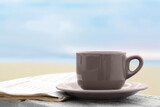 Ceramic cup of hot drink and newspaper on stone surface near sea in morning
