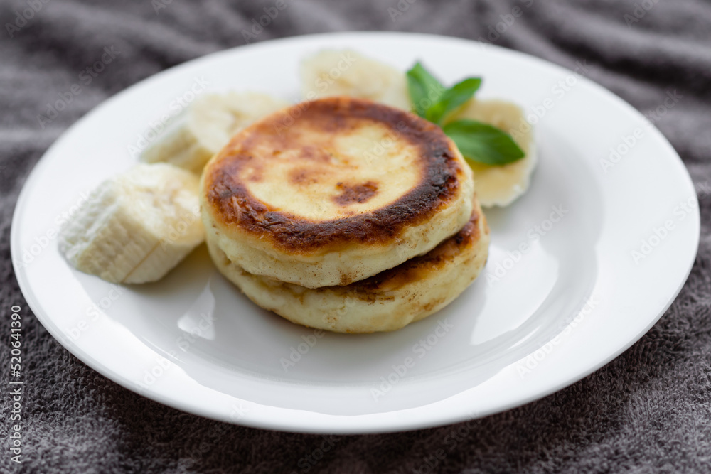 two curd fritters with sliced banana in a white plate