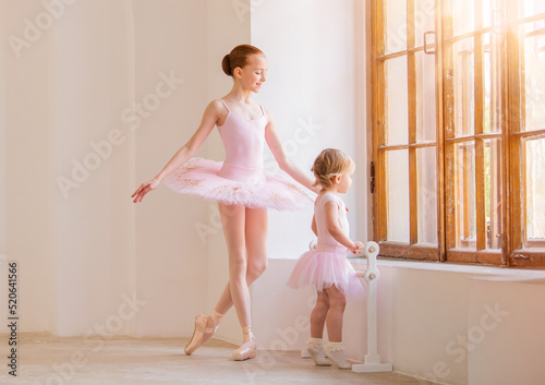 The older sister, a ballerina in a pink tutu and pointe shoes, shows the baby how to practice . © Maria Moroz