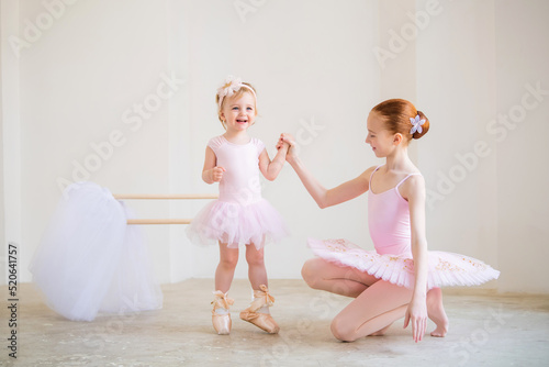 The older sister  a ballerina in a pink tutu and pointe shoes  shows the baby how to practice at the barre.
