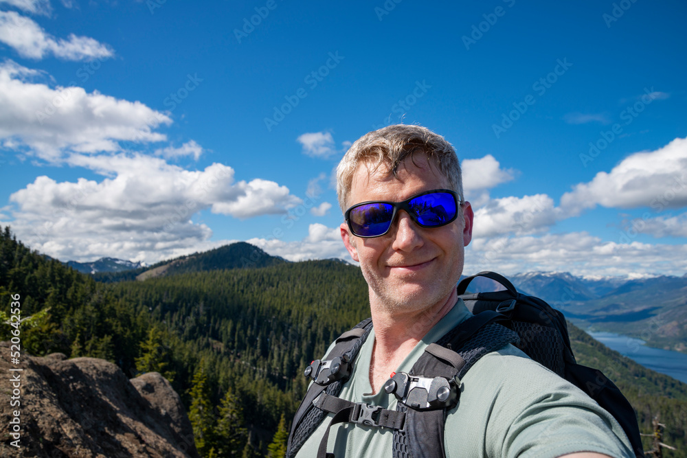 An adventurous athletic male hiker taking a selfie with a large lake and mountains in the background in the Pacific Northwest.