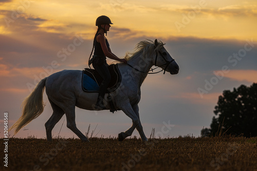 a young woman riding a white horse at sunset