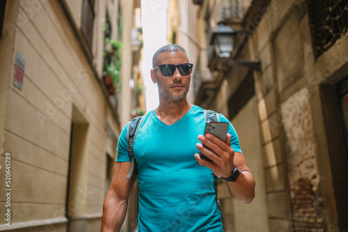 Happy male tourist phone user walking in old town alley an using smartphone. GPS maps, concept. Barcelona, Spain.