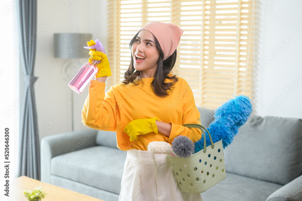 Young happy woman wearing yellow gloves and holding a basket of cleaning supplies in living room. Young happy woman wearing yellow gloves and holding a basket of cleaning supplies in living room.