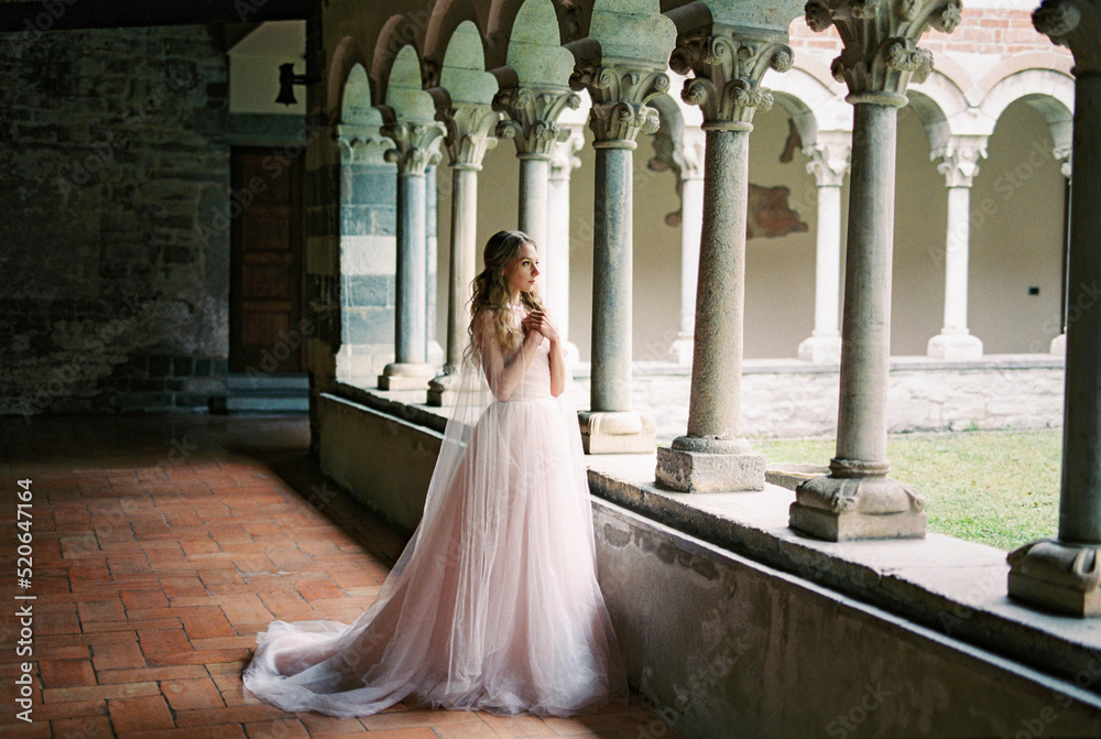 Bride stands with her arms folded across her chest on the terrace of an old villa. Lake Como, Italy