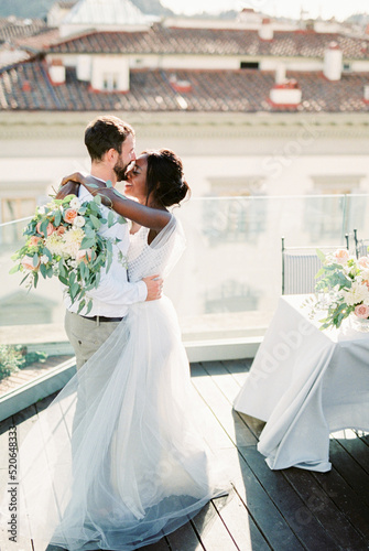 Groom hugs bride with a bouquet on the roof