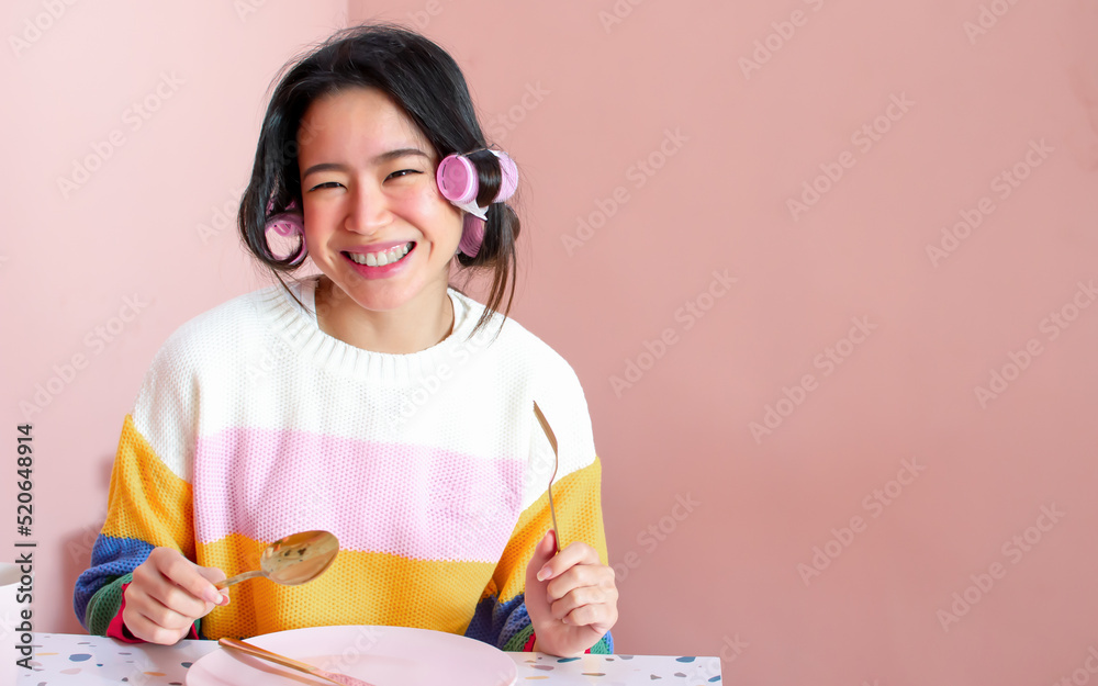 Portrait of asian beautiful woman rolling her hair and having breakfast at indoor pink cozy home, smiling with happiness. Beauty & Lifestyle Concept. Portrait of asian beautiful woman rolling her hair and having breakfast at indoor pink cozy home, smiling with happiness. Beauty & Lifestyle Concept.
