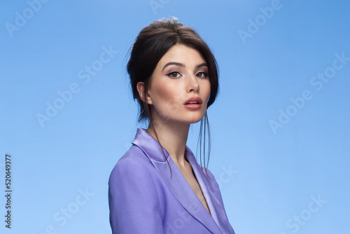 Brunette young woman in a stylish purple suit, looking at camera, isolated blue background.