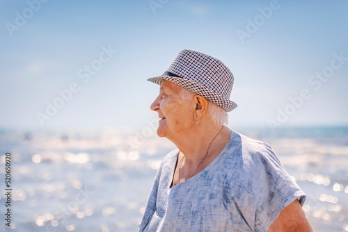 Portrait of an old gray-haired woman in a hat in profile against the background of the sea © tiplyashina