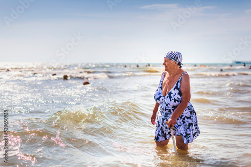 An old woman in a bathing suit with a cane went into the sea knee-deep
