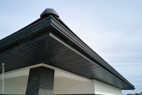 House corner with brown metal planks siding and roof with steel gutter rain system. Roofing, construction, drainage pipes installation photo