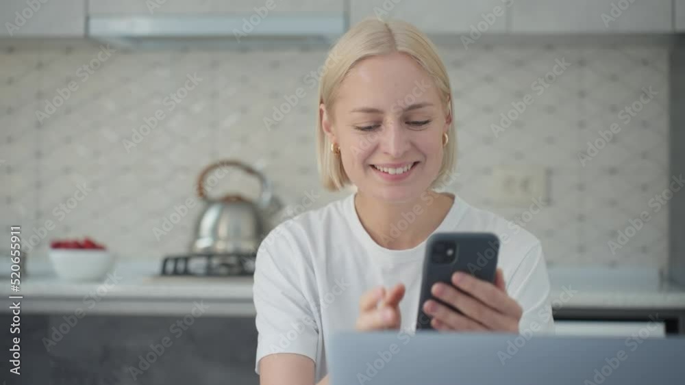 Joyful blonde woman waves bye in video call when sitting at laptop in kitchen Joyful blonde woman waves bye in video call when sitting at laptop in kitchen