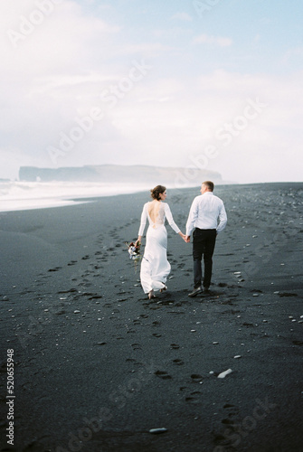Bride and groom walk on the black sand. Vik Beach  Iceland