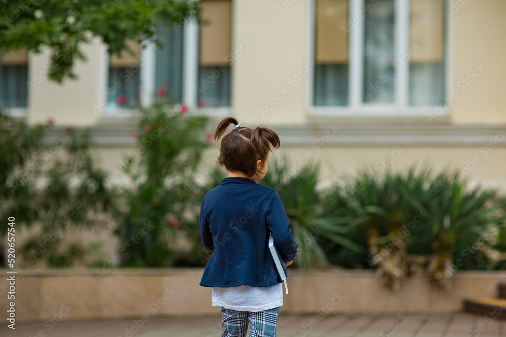 a little schoolgirl, in a school uniform, near the school building, with a diary in her hand a little schoolgirl, in a school uniform, near the school building, with a diary in her hand
