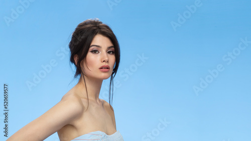 Beauty image of a cute brunette with bare shoulders with makeup and hairstyle, over blue background. Space for text.
