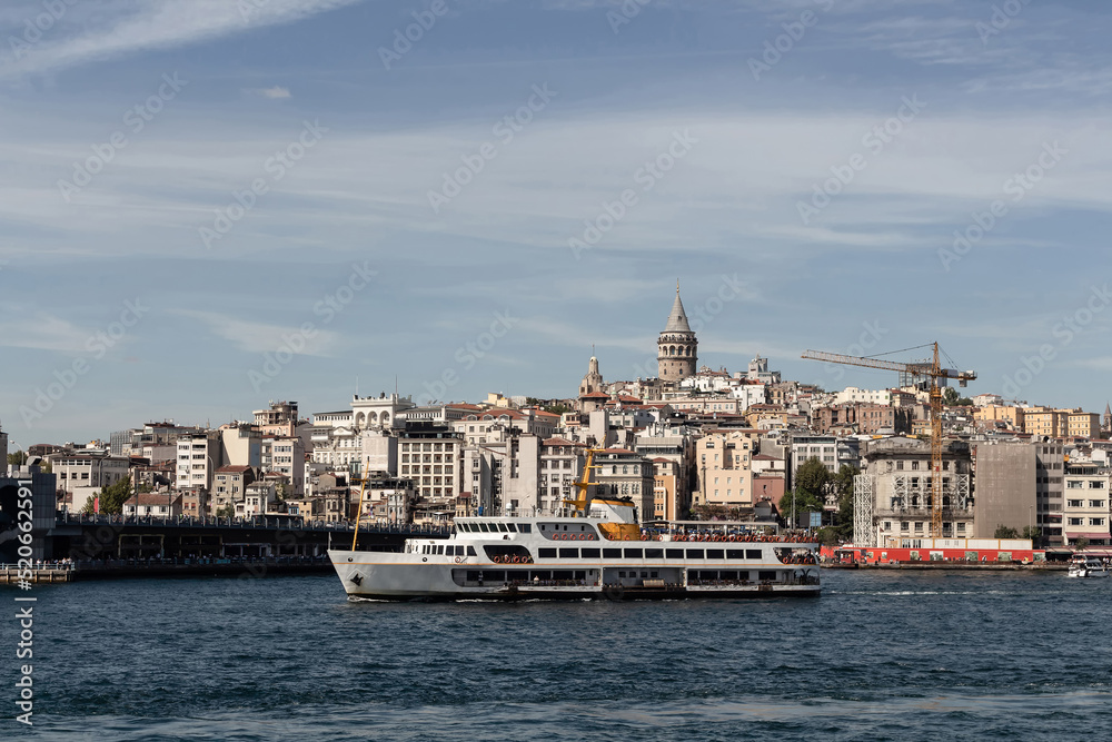 View of a traditional ferry boat on Golden Horn part of Bosphorus in Istanbul. Galata tower and Beyoglu district are in the view. It is a sunny summer day.