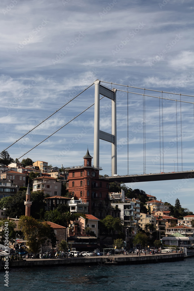 Obraz premium View of people walking by Bosphorus in Rumeli Hisari neighborhood on European side and FSM bridge in Istanbul. It is a sunny summer day. Beautiful travel scene.