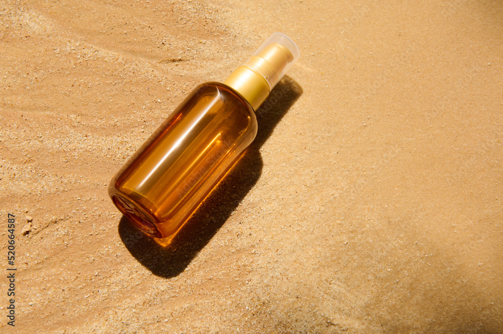 Unbranded dark glass bottle with SPF oil or sunscreen body lotion on sand beach background. Summer cosmetic concept. Unbranded dark glass bottle with SPF oil or sunscreen body lotion on sand beach background. Summer cosmetic concept.