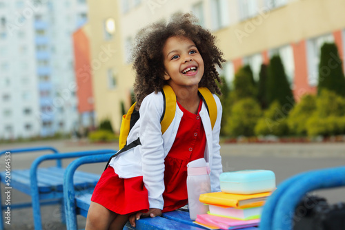 Cute Black schoolgirl eating lunch outdoors next the school. Healthy school breakfast for child.