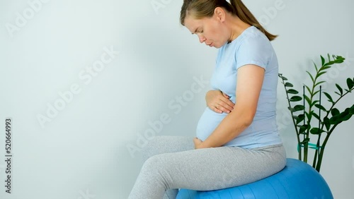 Pregnant woman feels contractions sitting on fitball and do breathing exercise to relief pain from labors. Pregnancy and childbirth. photo