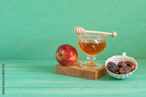 Fresh honey, date fruits, red apple for Jewish holiday Rosh Hashanah on green wooden background with copy space.
