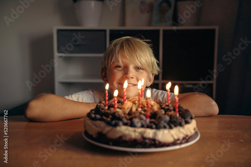 a boy, a child, a teenager, a blonde at the table in front of a cake with lit candles on his birthday