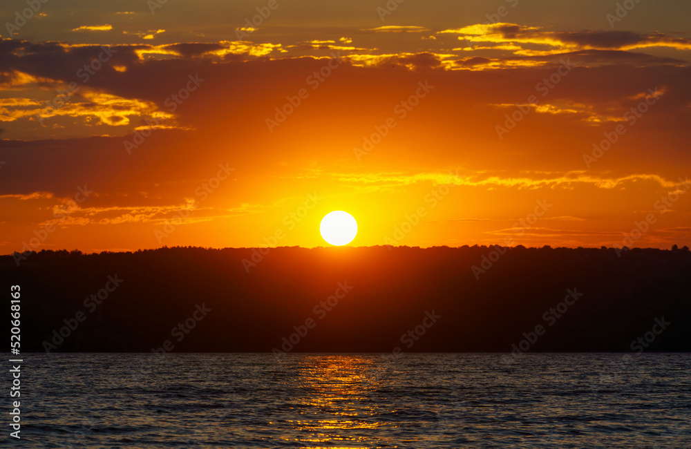 sunset over the lake, bright sun reflected in the waves, glare on the water, beautiful summer landscape